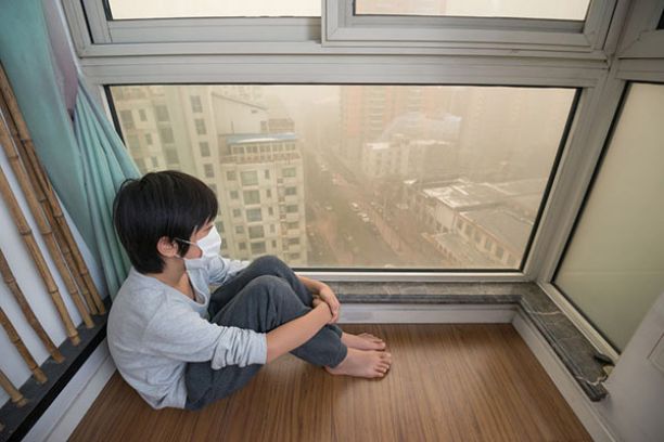 一个孩子在高层公寓里戴着口罩，看着烟雾弥漫的城市