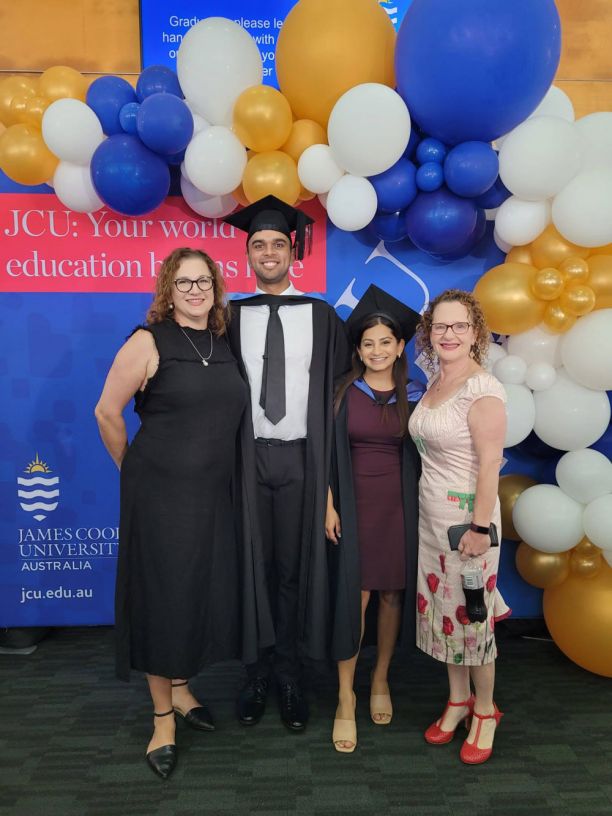 两个穿着礼服的大学毕业生和两个女人站在气球前